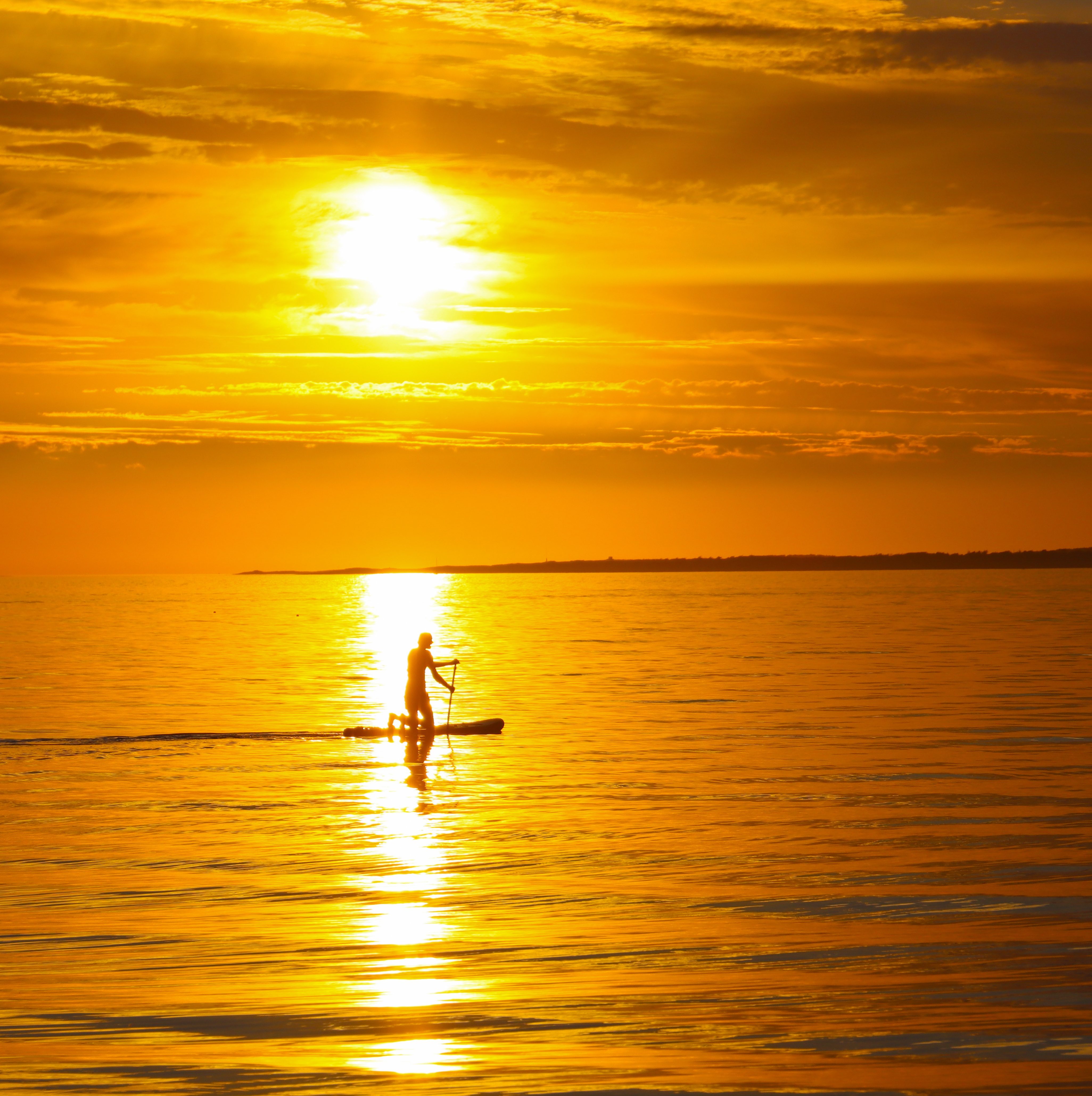 The sun setting over a paddle-boarding individual, who is floating on the sea.